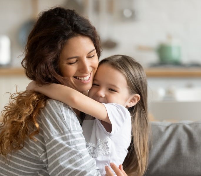 A mom hugging her daughter on a couch in their home.